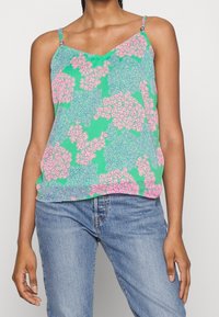 Kwiatowa koszulka na ramiączkach w zielonym materiale z różowymi i niebieskimi wzorami kwiatowymi, z cienkimi regulowanymi ramiączkami i luźnym krojem.