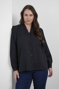 Blusa negra hecha de una tela suave, con escote con volantes, botones en la parte delantera y mangas largas. Textura sutil y corte relajado.