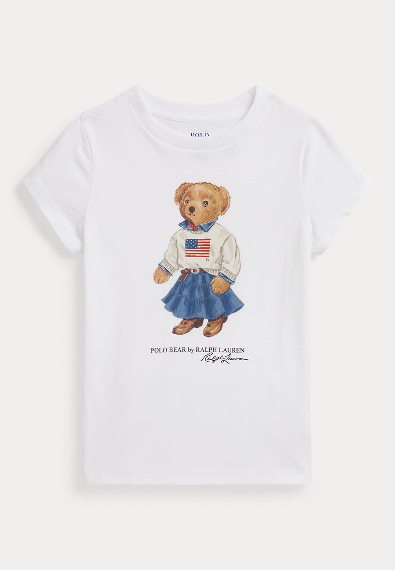 Balts kokvilnas T-krekls ar ilustrētu lāci džemperī ar Amerikas karogu, zila denima svārki un brūni zābaki. Paraksts zem attēla.