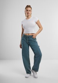 Tricou alb decupat, blugi albaștri largi cu buzunare frontale și adidași albi. Blugii au un finisaj decolorat și o croială lejeră.