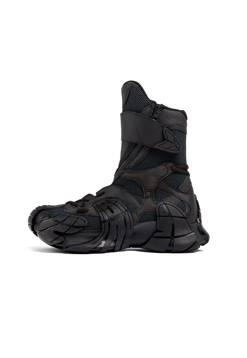 Svart atletisk boot med en texturerad mesh-ovandel, gummisula och justerbar rem. Har ett framträdande zigzag-mönster på sidan.