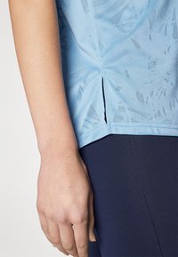 Lys blå treningsskjorte med et strukturert mønster, med en sidesplit og en tettsittende passform, kombinert med marineblå leggings.