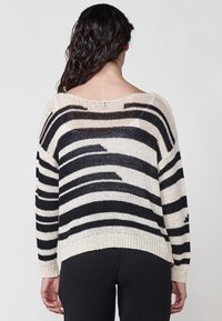 Pulover cu dungi în crem �și negru, având o croială lejeră, gât larg și umeri lăsați. Textură tricotată cu margine și manșete ribbate.