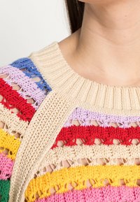 Wielokolorowy sweter na szydełku z szerokim beżowym ściągaczem przy szyi, ozdobiony poziomymi paskami w kolorze niebieskim, purpurowym, czerwonym, różowym, żółtym i zielonym.