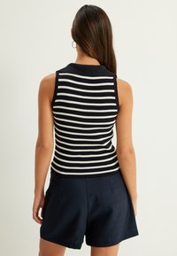 Canotta a righe blu e bianche senza maniche con texture a coste e colletto, abbinata a pantaloni corti blu. La vista posteriore mostra il design aderente.