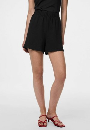 Shorts noirs avec taille élastique et surface texturée, à coupe ample et jambes larges, assortis à des sandales rouges à brides.