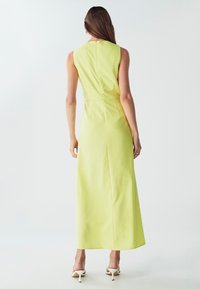 Bežėnė, grindų ilgio suknelė ryškiai geltonos spalvos audinio. Yra prisitaikanti silueto forma ir užtrauktukas nugaroje. Lygus paviršius su minimaliais detalėmis.