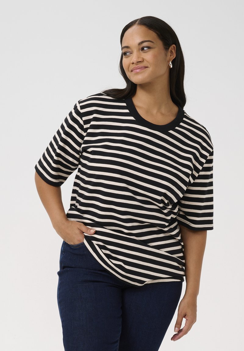 Stripet t-shirt med sorte og cremefarvede vandrette striber, rund halsudskæring, korte ærmer og en afslappet pasform, parret med mørkeblå jeans.