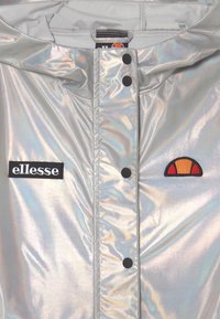 Irydnescentna srebrna kurtka z czarnym logo 'ellesse' i czerwoną oraz pomarańczową naszywką. Dwa czarne zatrzaski z przodu.
