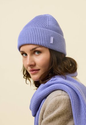 Lavender ribbed knit beanie with matching scarf, featuring a tag on the hat. Soft texture, form-fitting shape, and warm fabric.