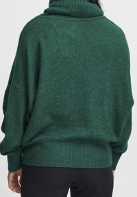 Maglione verde, oversize, con collo alto realizzato in un morbido tessuto testurizzato. Presenta un colletto e dei polsini a costine, con una vestibilità rilassata e cadente.