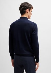 Navy blue knitted sweater with long sleeves, ribbed cuffs and hem, featuring a classic crew neckline, displayed from a rear view.