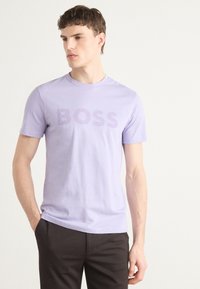 T-shirt en coton lavande avec des manches courtes et un logo "BOSS" audacieux, légèrement plus foncé, à l'avant. Design simple et ajusté.