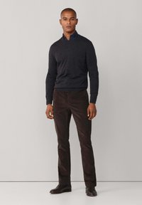 Tmavě šedý svetr přes světle modrou košilí s límečkem, doplněný tmavě hnědými kalhotami a černými botami, vyznačující se přiléhavým střihem a hladkou texturou.