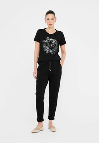 Sort bomulds t-shirt med sølvfarvet blomsterbroderi, parret med sorte sweatpants med elastisk talje. Sættet har en afslappet pasform og opkrøllede ærmer.