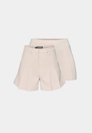 Béžové plisé šortky z lehké tkaniny s pasem a zadní kapsou. Za nimi jsou zobrazeny hladké přiléhavé šortky stejné barvy.