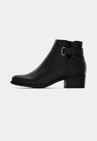 Črni gležnjar iz gladkega usnja s prešitim zadnjim delom, z zlatimi kovinskimi dodatki in masivnim peto. Stranski zipper za enostavno obuvanje.