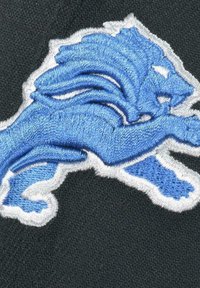 Schwarzer Stoff mit einem gestickten blauen Löwenlogo und weißen Details. Der Löwe befindet sich in einer dynamischen, springenden Pose.