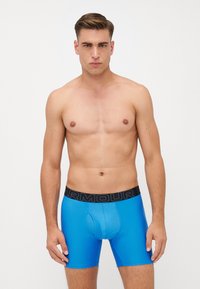 Boxeri scurți, colorați în albastru, fabricați dintr-un material neted, cu un elastic negru inscripționat. Designul include un compartiment frontal de susținere și o formă ajustată.