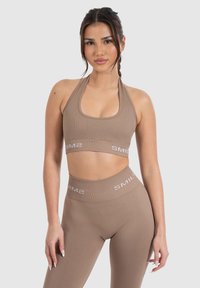 Bruin geribbelde sportbeha met een halternek en logo-band, gecombineerd met bijpassende hoge taille leggings met een soortgelijk logodetail.