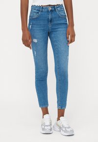 Vaqueros de denim azul de corte skinny, con roturas, diseño de cinco bolsillos y una cintura de altura media. La tela tiene una textura suave con un ligero estiramiento.