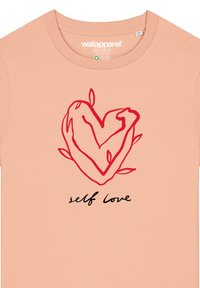 Perzikkleurig katoenen T-shirt met een rode hartillustratie omringd door bladeren en de tekst "zelfliefde" in zwart onder het ontwerp.