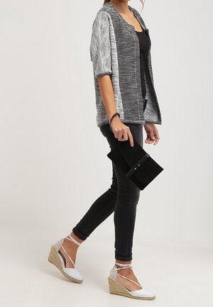 Šedý texturovaný otevřený kardigan, černý top, černé skinny džíny, bílé espadrilky na klínu s kotníkovými vazy a černá kabelka.