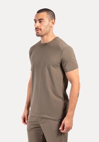 Koszulka z krótkim rękawem, okrągłym dekoltem w stonowanym oliwkowym zielonym kolorze, wykonana z gładkiego, lekkiego materiału. Zawiera subtelne logo na końcu.