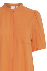 Oranžinė trumpa rankovėbluzė su mandarinų tipo apykakle, priekinėmis krūtinės kišenėmis ir sagstoma apykakle, rodomas nuo viršutinės liemens dalies.