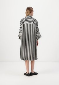 Hame dress bergaris hitam dan putih, dengan lengan besar dan potongan santai, dilengkapi dengan kolar dan panjang hingga tengah betis.