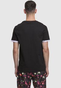 Juoda trumpomis rankovėmis su apvalia iškirpte ir kontrastingomis baltomis rankogaliais marškinėliai, derinami su daugiaspalviais šortais su palmės ir grafiniu raštais.