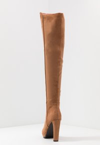 Kozaki do kolan, brązowe z sztucznego zamszu, o eleganckim wzornictwie, wysokim obcasie w kształcie szpilki oraz gładkiej teksturze. Posiadają dopasowaną sylwetkę i minimalne zdobienia.