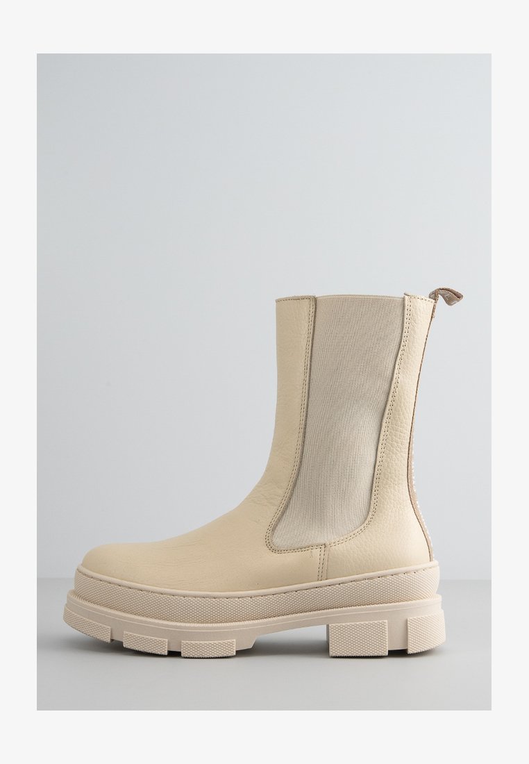 Beżowy botek za kostkę z gładkiej skórzanej cholewki i elastycznymi bocznymi panelami. Posiada grube, teksturowane podeszwy z bieżnikiem oraz pętlę do zakupu.