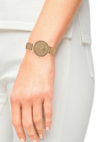 Ronde horloge met een tan kleurige stoffen strap en een rose-gouden kast. Houtpatroon wijzerplaat met zilveren uurmarkeringen en een minimalistisch design.