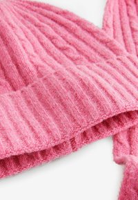 Roze gebreide muts met ribbelstructuur, gemaakt van zacht materiaal, met een brede rand en duidelijke verticale lijnen in de stof.
