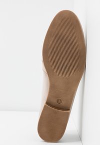 Semelle de chaussure beige avec motifs antidérapants texturés au talon et à la plante du pied, taille 37 indiquée près de la voûte plantaire, positionnée sur un fond blanc.