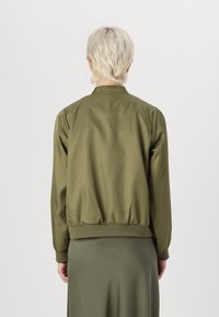 Giacca bomber verde oliva con una texture liscia, orlo e polsini a costine. Design semplice senza hardware visibile o motivi sul retro.