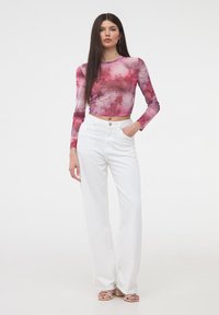 Top cropped a maniche lunghe di colore rosa con un motivo ad acquerello, abbinato a pantaloni bianchi a vita alta e a gamba ampia, e sandali con tacco di un rosa chiaro.