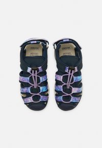 Sandales bleu marine au design respirant, avec des sangles multicolores en violet et bleu, maintenues par des lacets élastiques et une fermeture Velcro.