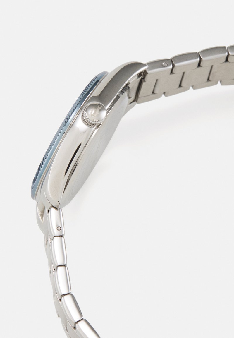 Montre en acier inoxydable argenté avec une lunette bleue ronde, une couronne texturée et un bracelet à maillons, présentant un design élégant et poli.