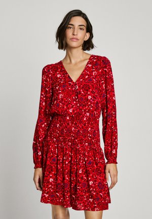 Robe florale rouge avec manches longues, décolleté en V et taille froncée. Présente des motifs vibrants dans des teintes de rouge, bleu et blanc.