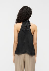 Μαύρο τοπ halter από υφασμά τινη ύφανση με ραβδώσεις. Δέσιμο στο πίσω μέρος σχηματίζει φιόγκο. Ροή με ελαφρώς κυρτή γραμμή στο τελείωμα.