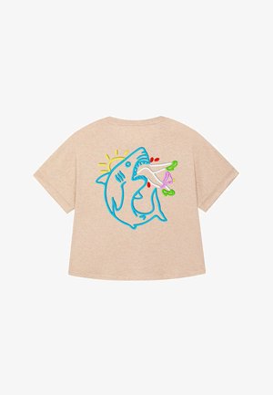T-shirt beige con vestibilità ampia. Presenta uno squalo blu ricamato con un sole, che tiene in mano oggetti colorati. Maniche corte e texture morbida.