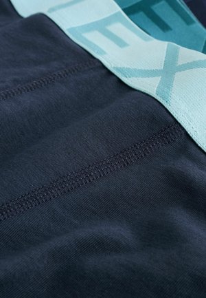 Pogled od blizu na mornarsko plavu tkaninu s detaljnim šivanjem i svijetloplavom elastičnom trakom koja dijelom prikazuje tekst.