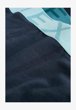 Pogled od blizu na mornarsko plavu tkaninu s detaljnim šivanjem i svijetloplavom elastičnom trakom koja dijelom prikazuje tekst.