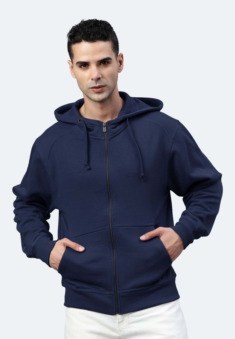 Felpa con zip di colore blu navy, realizzata in materiale morbido, dotata di cappuccio, tasche frontali e polsini a costine con cordini per una vestibilità regolabile.