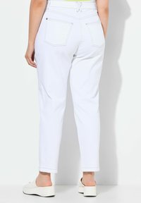 Pantalones blancos de cintura alta con pierna ajustada, que cuentan con costuras en contraste, dos bolsillos traseros y bajos enrollados. Combinados con zuecos de plataforma blancos.