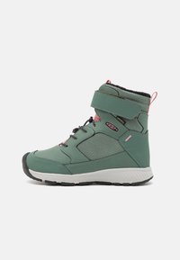 Groene waterdichte boot met een hoge enkel, textuurpanelen aan de zijkanten, zwarte binnenvoering, roze accenten en een witte zool met rubberen profiel.