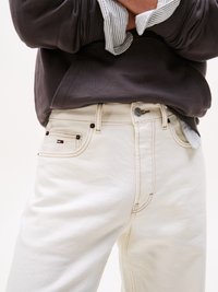 Hvite denimbukser med kontrastsøm og sidelommer, kombinert med en mørkegrå sweatshirt og en lys stripete skjorte under.