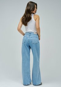 Světlé modré široké džíny s vysokým pasem, které mají dvě zadní kapsy a viditelný horizontální šev. Materiál vypadá jako denim.